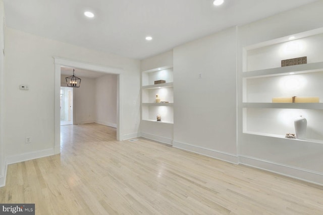 empty room featuring wood finished floors, built in shelves, an inviting chandelier, baseboards, and recessed lighting