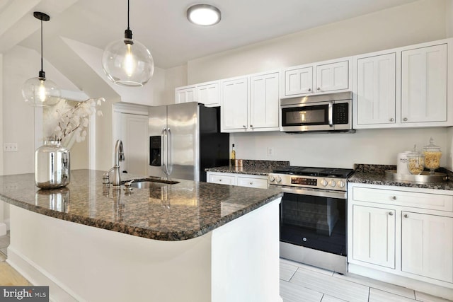 kitchen featuring decorative light fixtures, dark stone countertops, stainless steel appliances, and a sink