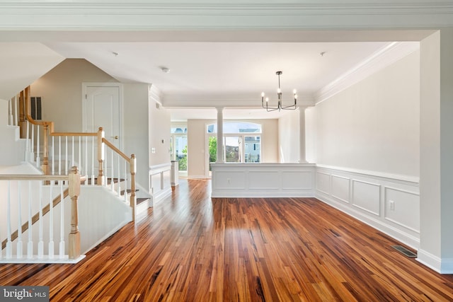 unfurnished room with crown molding, wainscoting, wood finished floors, and a notable chandelier