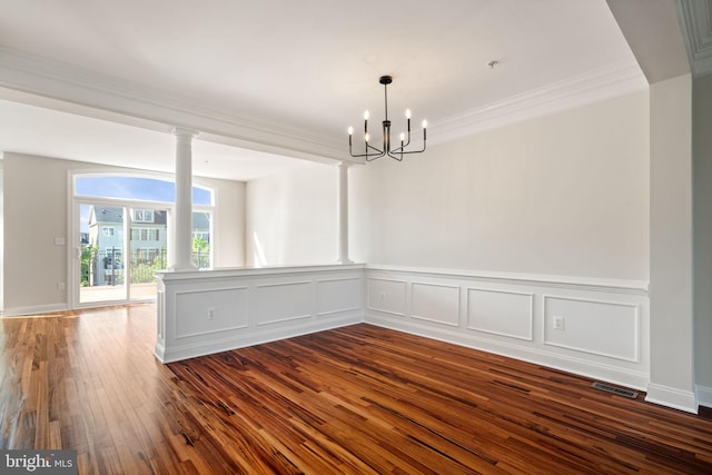 spare room with a notable chandelier, decorative columns, dark wood-type flooring, visible vents, and ornamental molding