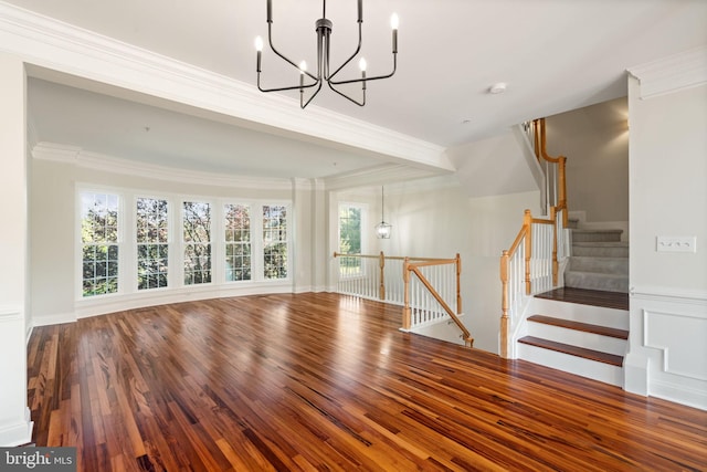 unfurnished living room featuring ornamental molding, stairs, wood finished floors, and a chandelier