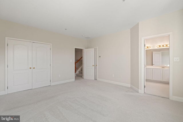 unfurnished bedroom with baseboards, light colored carpet, ensuite bathroom, and a closet