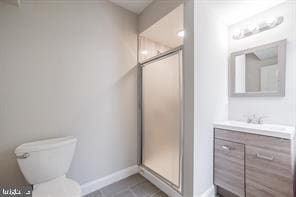 bathroom featuring baseboards, toilet, vanity, tile patterned floors, and a stall shower