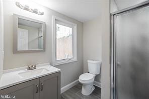 bathroom featuring toilet, a stall shower, baseboards, and vanity