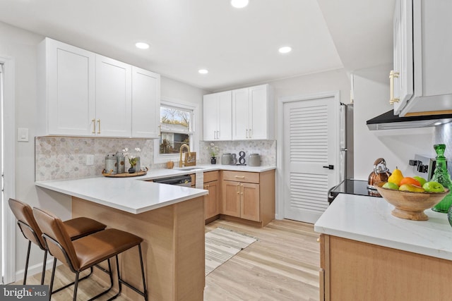 kitchen featuring light wood finished floors, a peninsula, backsplash, under cabinet range hood, and a breakfast bar area