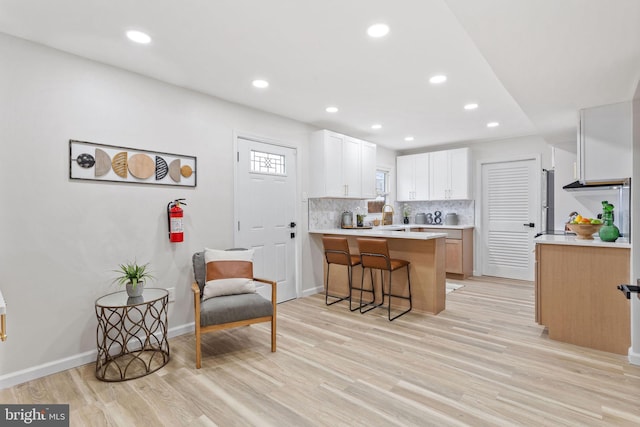 kitchen featuring tasteful backsplash, a breakfast bar area, light wood-style flooring, white cabinets, and a peninsula