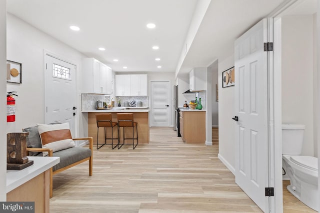 kitchen featuring tasteful backsplash, light wood-type flooring, a kitchen bar, a peninsula, and white cabinetry
