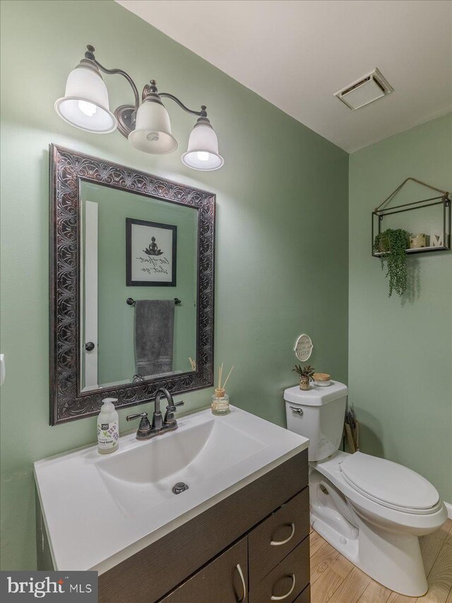 bathroom with toilet, wood finished floors, vanity, and visible vents