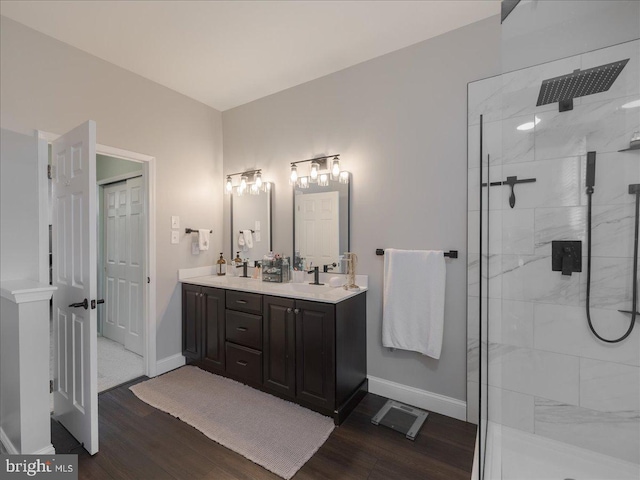 full bath with wood finished floors, double vanity, tiled shower, and baseboards