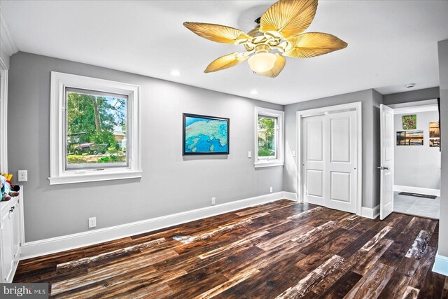 unfurnished bedroom featuring baseboards, dark wood-style flooring, multiple windows, and a closet