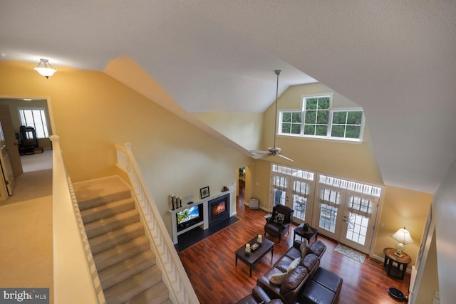living room featuring ceiling fan, stairway, wood finished floors, a lit fireplace, and high vaulted ceiling