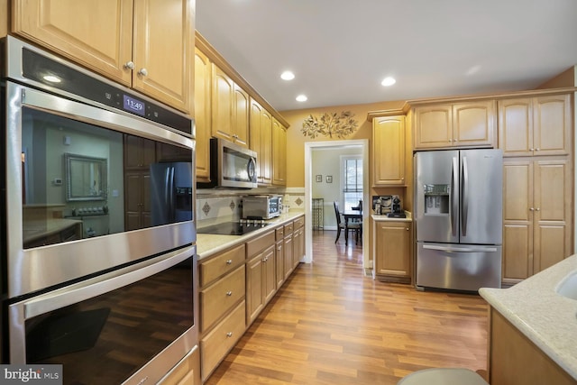 kitchen with tasteful backsplash, light countertops, light brown cabinetry, stainless steel appliances, and light wood-style flooring