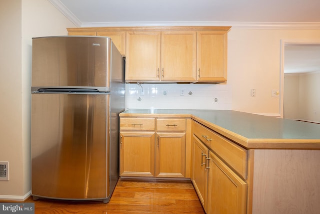 kitchen featuring ornamental molding, light wood-type flooring, freestanding refrigerator, a peninsula, and backsplash