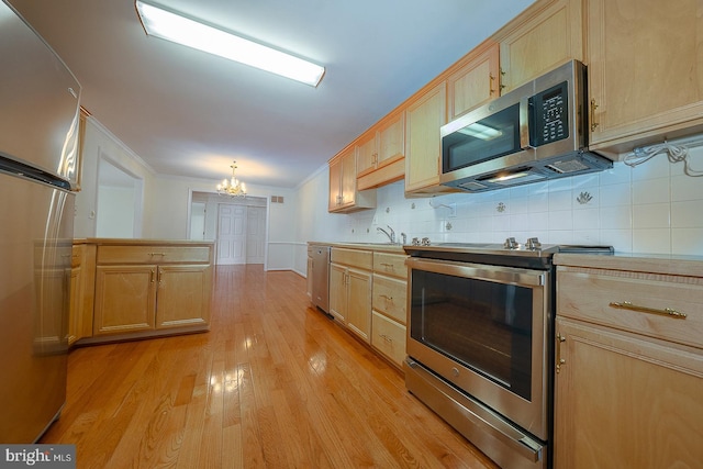 kitchen with crown molding, light wood-style flooring, appliances with stainless steel finishes, decorative backsplash, and a notable chandelier