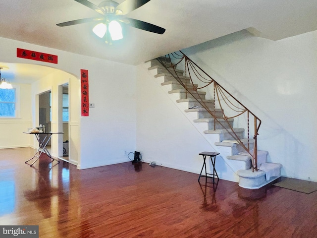 unfurnished living room with arched walkways, ceiling fan, stairs, and wood finished floors
