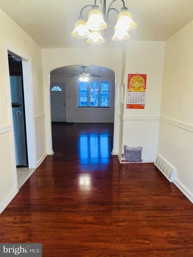 hall with a chandelier, arched walkways, wood finished floors, and visible vents