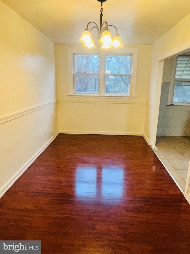 unfurnished dining area featuring plenty of natural light, an inviting chandelier, and wood finished floors