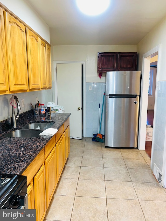 kitchen with range, dark stone countertops, light tile patterned floors, freestanding refrigerator, and a sink