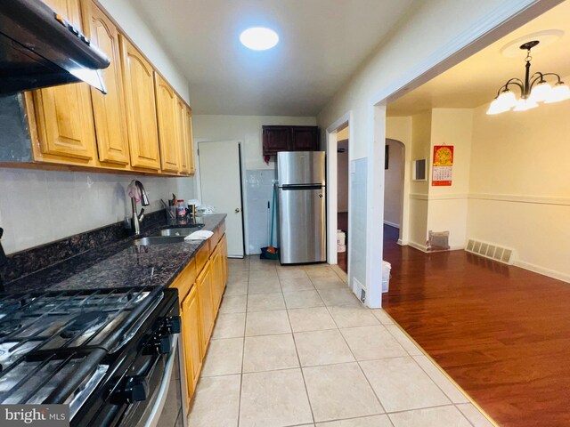 kitchen featuring freestanding refrigerator, under cabinet range hood, visible vents, arched walkways, and a sink