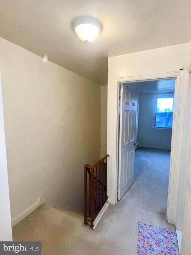 hall featuring baseboards, an upstairs landing, and light carpet