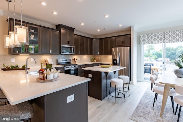 kitchen with dark brown cabinetry, a breakfast bar, light countertops, stainless steel appliances, and a sink