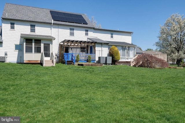 rear view of property with roof mounted solar panels, a pergola, a yard, and a sunroom