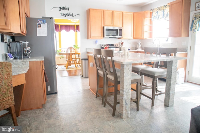 10861 Smugglers Notch Ct, White Plains, MD 20695 - kitchen featuring stainless steel appliances, light countertops, a kitchen breakfast bar, light brown cabinets, and light flooring