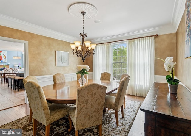 dining area with light wood finished floors, a decorative wall, crown molding, wainscoting, and a chandelier