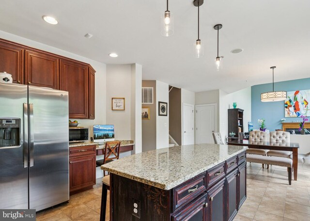 kitchen featuring a center island, light stone counters, stainless steel appliances, decorative light fixtures, and visible vents
