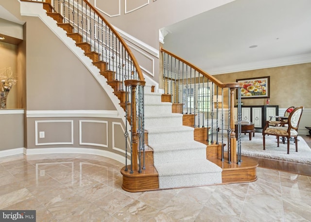 stairway featuring crown molding, a decorative wall, marble finish floor, and baseboards
