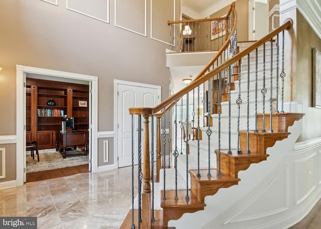 staircase with a towering ceiling, marble finish floor, ornamental molding, and a decorative wall