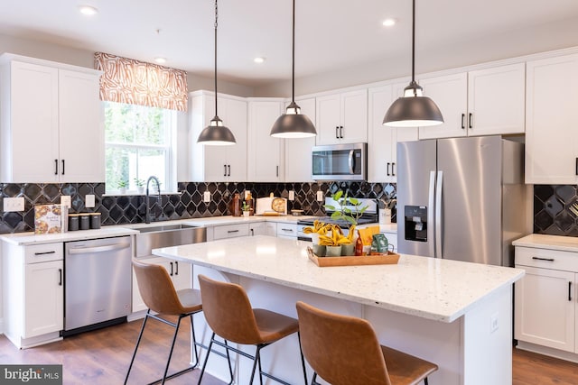 kitchen with a breakfast bar area, backsplash, a center island, white cabinets, and stainless steel appliances