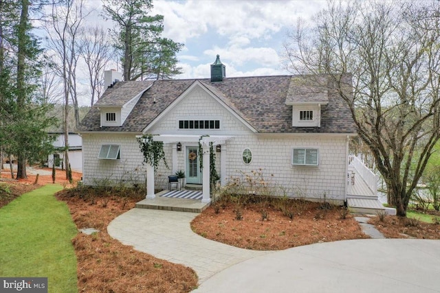cape cod-style house with a front lawn, a shingled roof, and a chimney