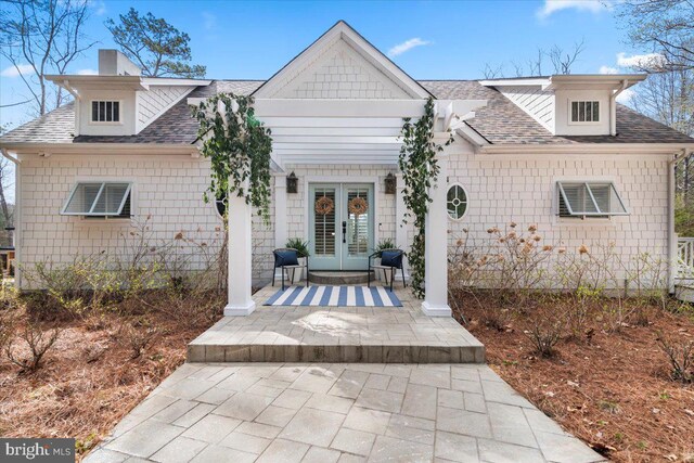 view of front of home with french doors, a chimney, and a shingled roof