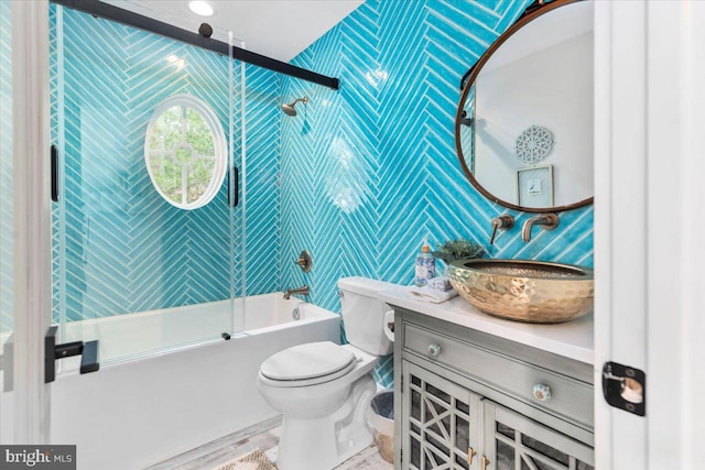 bathroom featuring bath / shower combo with glass door, toilet, vanity, and wallpapered walls