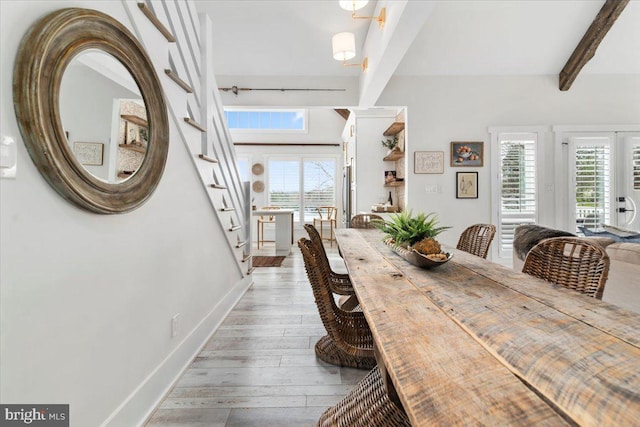 dining space featuring light wood finished floors, beamed ceiling, baseboards, and stairway