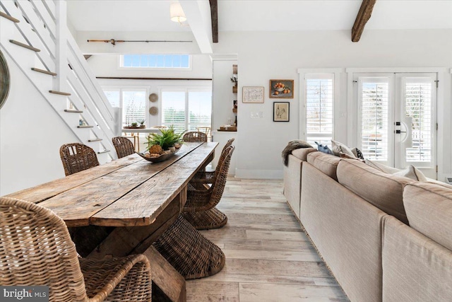 dining space with stairs, light wood-style floors, baseboards, and beamed ceiling