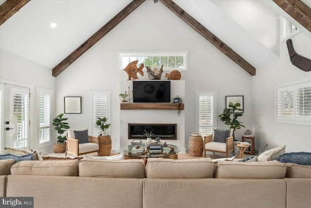 living room with high vaulted ceiling, a glass covered fireplace, plenty of natural light, and beamed ceiling