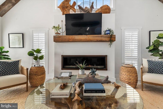 living room featuring a healthy amount of sunlight, high vaulted ceiling, baseboards, and a glass covered fireplace