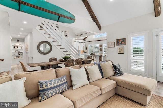living area featuring a healthy amount of sunlight, stairs, vaulted ceiling with beams, and wood finished floors