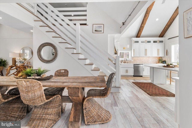 dining room featuring light wood-type flooring, high vaulted ceiling, beam ceiling, and stairway