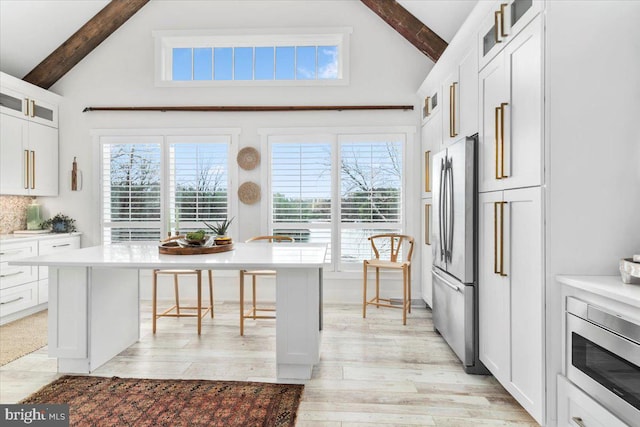 kitchen with beamed ceiling, high vaulted ceiling, appliances with stainless steel finishes, and a breakfast bar area