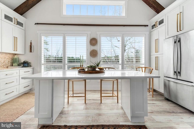 kitchen featuring beamed ceiling, a kitchen breakfast bar, a healthy amount of sunlight, light countertops, and stainless steel fridge