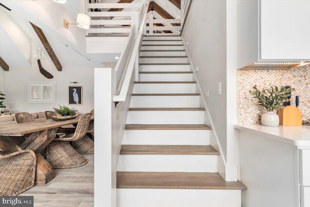 staircase with beamed ceiling and wood finished floors
