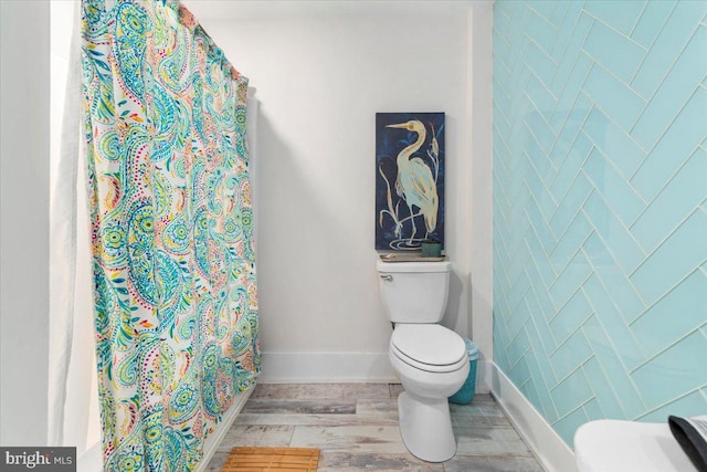 bathroom with curtained shower, baseboards, toilet, and wood finished floors