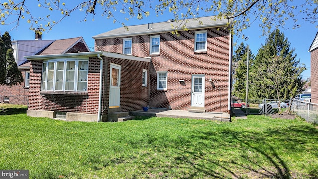 rear view of property with brick siding, a yard, entry steps, and fence