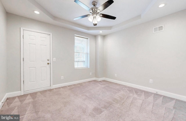 unfurnished room with ceiling fan, light colored carpet, visible vents, a raised ceiling, and baseboards