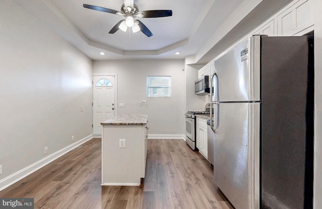 kitchen with a tray ceiling, white cabinets, appliances with stainless steel finishes, and a kitchen island