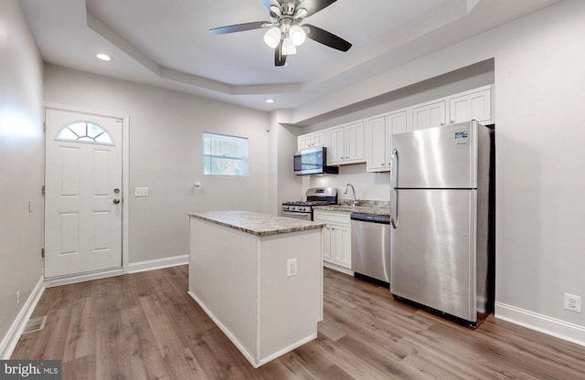 kitchen with a raised ceiling, a center island, white cabinets, ceiling fan, and stainless steel appliances