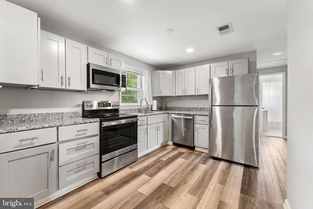 kitchen featuring recessed lighting, light stone counters, stainless steel appliances, light wood finished floors, and visible vents